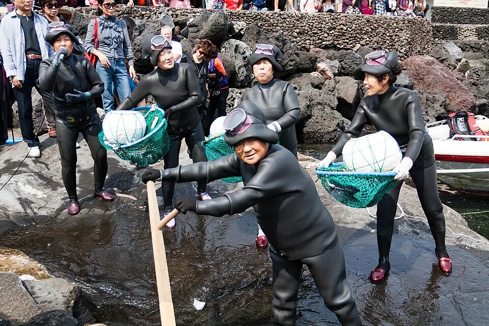 Grupo de haenyeo de Jeju junto al mar con sus trajes de buceo, flotadores y redes de recolección.